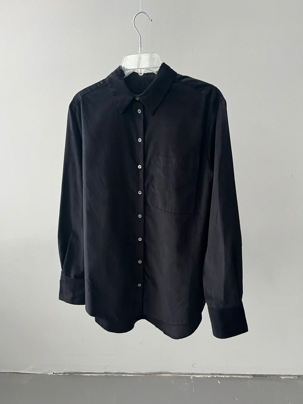 A phone photo of a black shirt on a hanger against a white wall